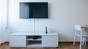 A modern room with a flat-screen TV mounted on the wall, a white desk with a drawer, a chair, and a wooden table. - Lisboa Almirante Reis Downtown Flat E (Lisbon)