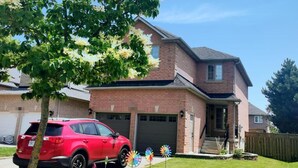 A two-story house with a garage, a red SUV parked in front, and a tree with white flowers.