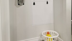A room with a white wall, a hanging landscape painting, a whiteboard, and a laundry basket with yellow and red items.