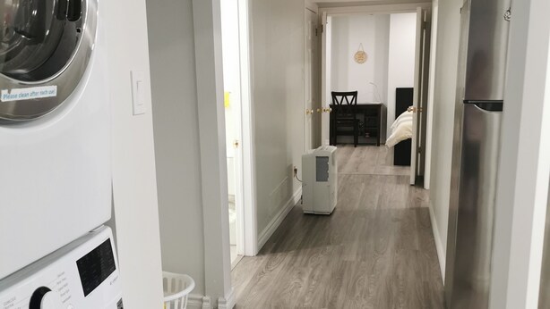 A laundry room with a front-loading washer and dryer, a refrigerator, and a dining area in the background.