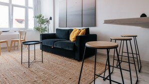 A modern living room with a dark sofa, two round tables, a large abstract painting, and a view of the outside through a window.