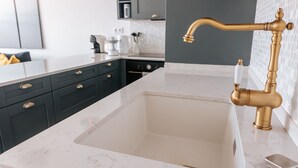 A modern kitchen with a white marble countertop, dark cabinetry, and a gold faucet.