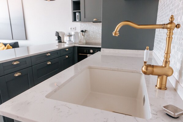 A modern kitchen with a white marble countertop, dark cabinetry, and a gold faucet. - Lisboa Almirante Reis Central Flat D (Lisbon)