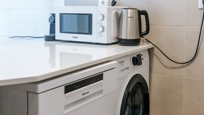 A compact laundry area with a washing machine, a microwave, and a coffee maker.