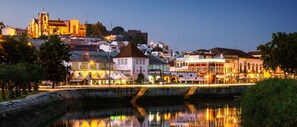 Paisagem urbana à beira-mar com edifícios históricos, uma igreja destacada e uma ponte sobre um rio calmo.