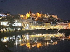 Vista noturna de uma cidade com uma igreja imponente e edifícios refletidos em um corpo de água.
