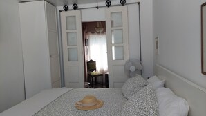 A bedroom with a bed, a hat on the bed, a chair, a fan, and a door with frosted glass panels. - Beach Wave Melides Villa (Grandola)