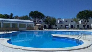 A swimming pool with a covered area and a building in the background. - Nice Terrace and Pool Alvor Flat (Portimão)