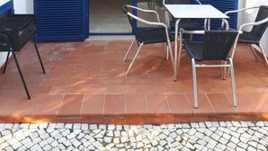 A patio with a table and chairs, a grill, and blue shutters on a building. - Nice Terrace and Pool Alvor Flat (Portimão)