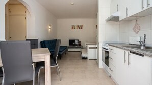 A compact kitchen with white cabinets, a dining area with a table and chairs, and a TV in the background. - Nice Terrace and Pool Alvor Flat (Portimão)