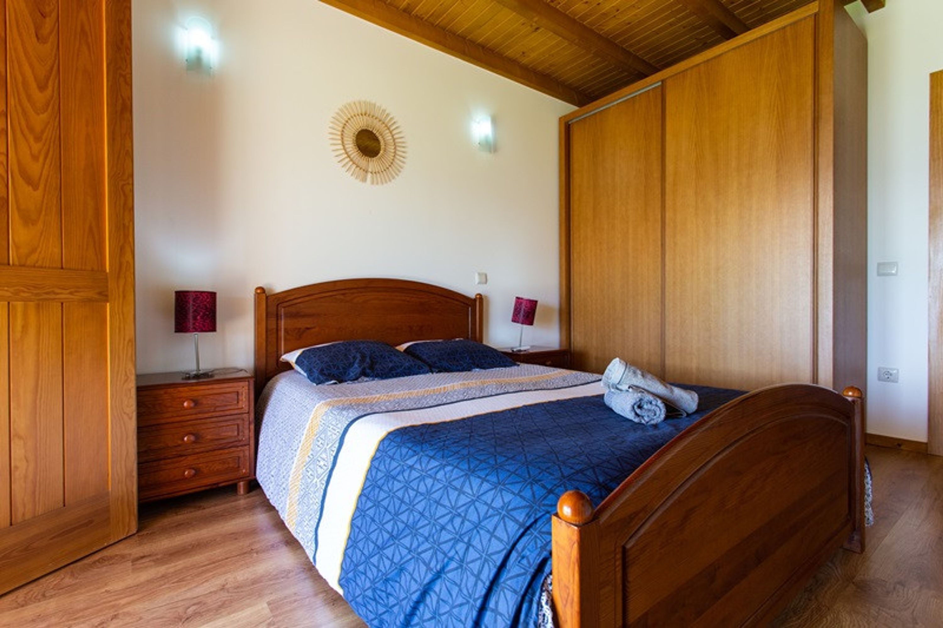Un dormitorio con una cama de madera, dos mesitas de noche, una lámpara de pared y un armario de madera.