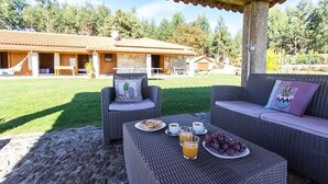 Un espacio de estar al aire libre cubierto con mobiliario de mimbre, una mesa con alimentos para el desayuno y un edificio con tejado de tejas al fondo.