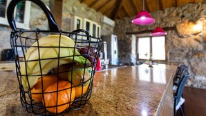 Una cocina con una cesta de frutas sobre la encimera, paredes de piedra y lámparas colgantes.