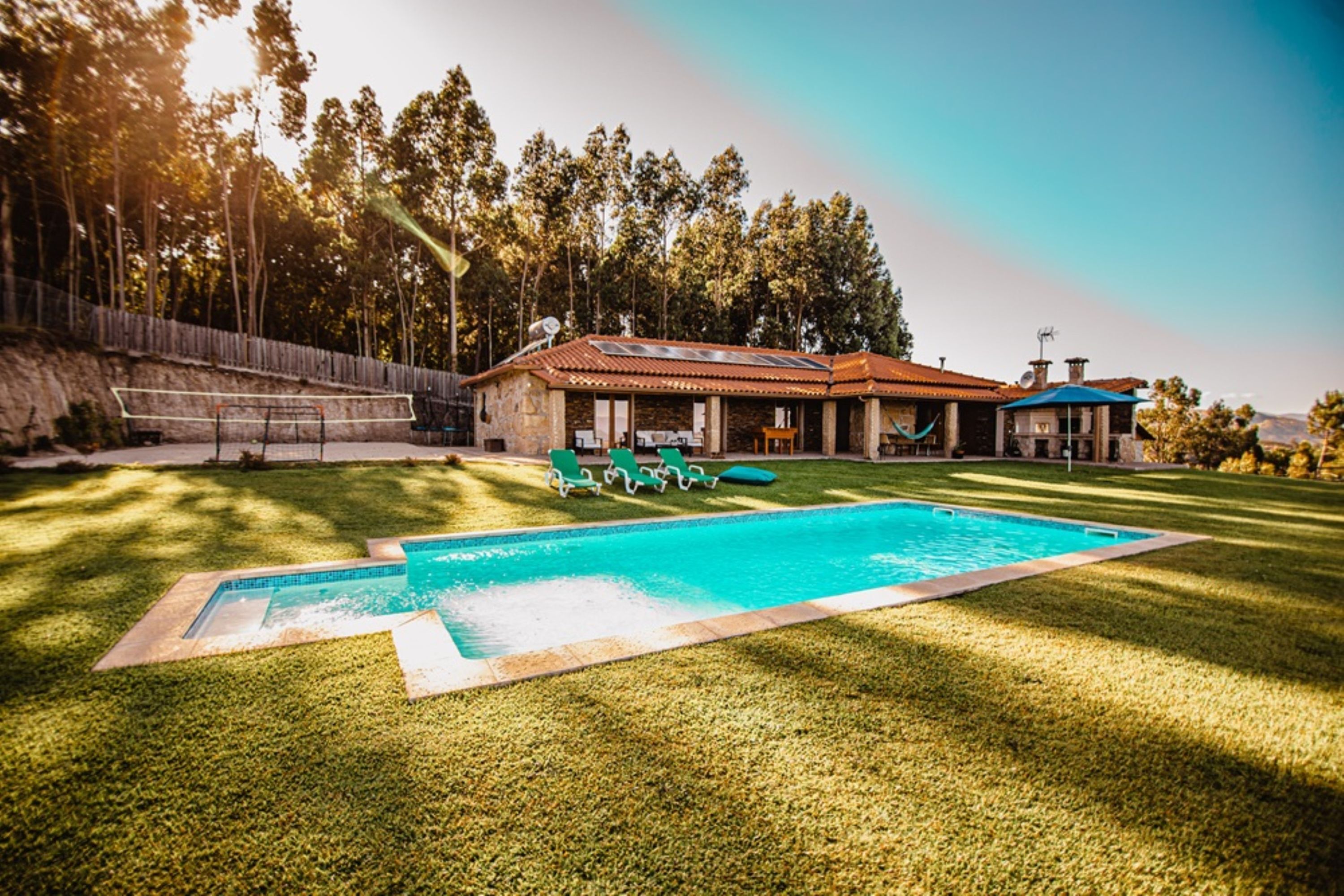 Ein Garten mit Schwimmbad, grüner Rasenfläche und einem Haus mit rotem Dach.
