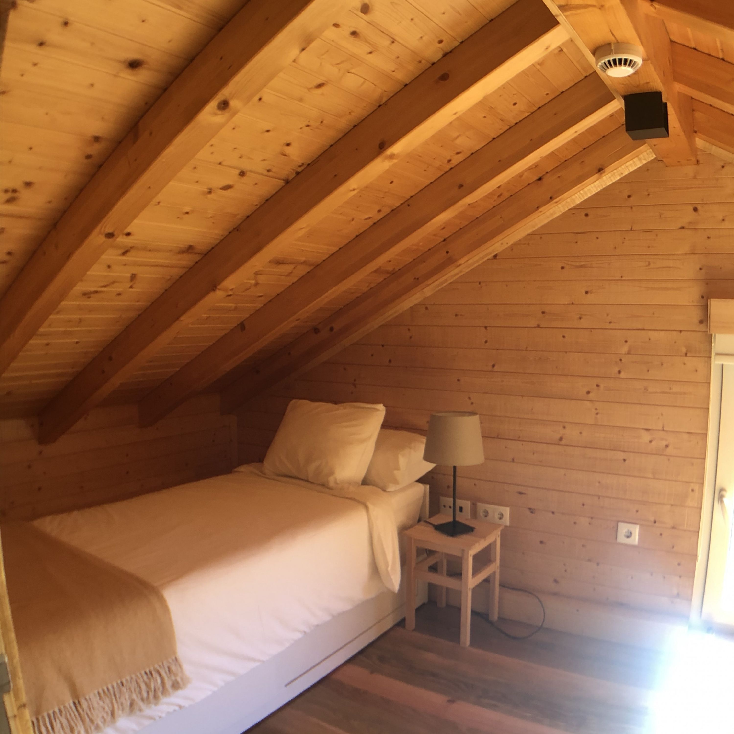 Camera da letto in una baita di legno, con un letto, un comodino e una lampada.