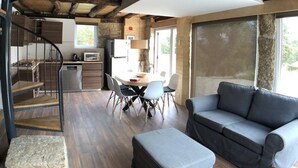 A rustic interior with exposed wooden beams, a spiral staircase, a dining area with a round table and chairs, a sofa, and a large window. - Vila Espigueiro I in Bustelo (Penafiel)