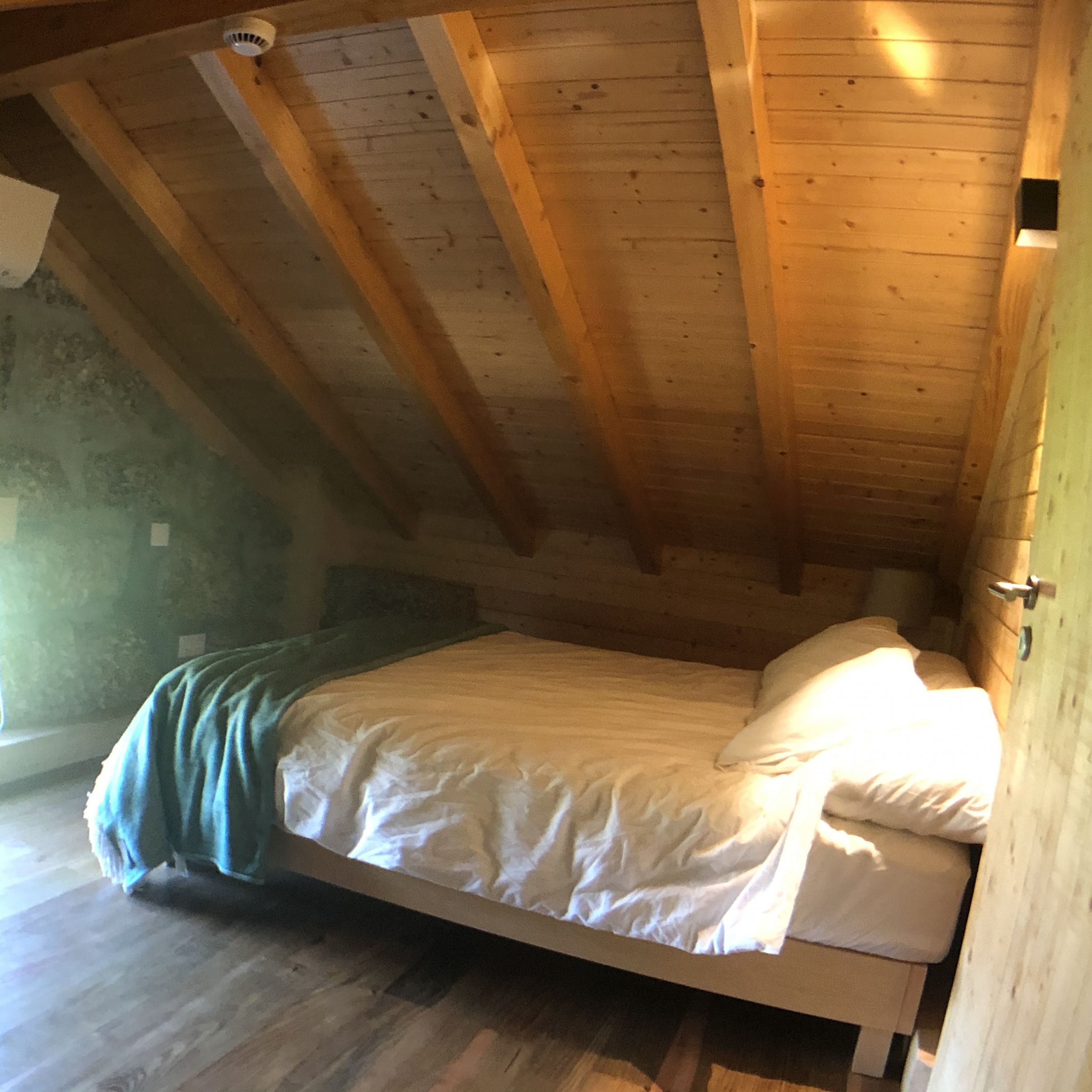 A single bed in a loft-style room with wooden beams on the ceiling and a sloped roof.