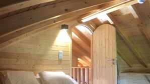 A wooden interior with a sloped ceiling, a bed with pillows, and a visible door leading to another room. - Vila Espigueiro I in Bustelo (Penafiel)