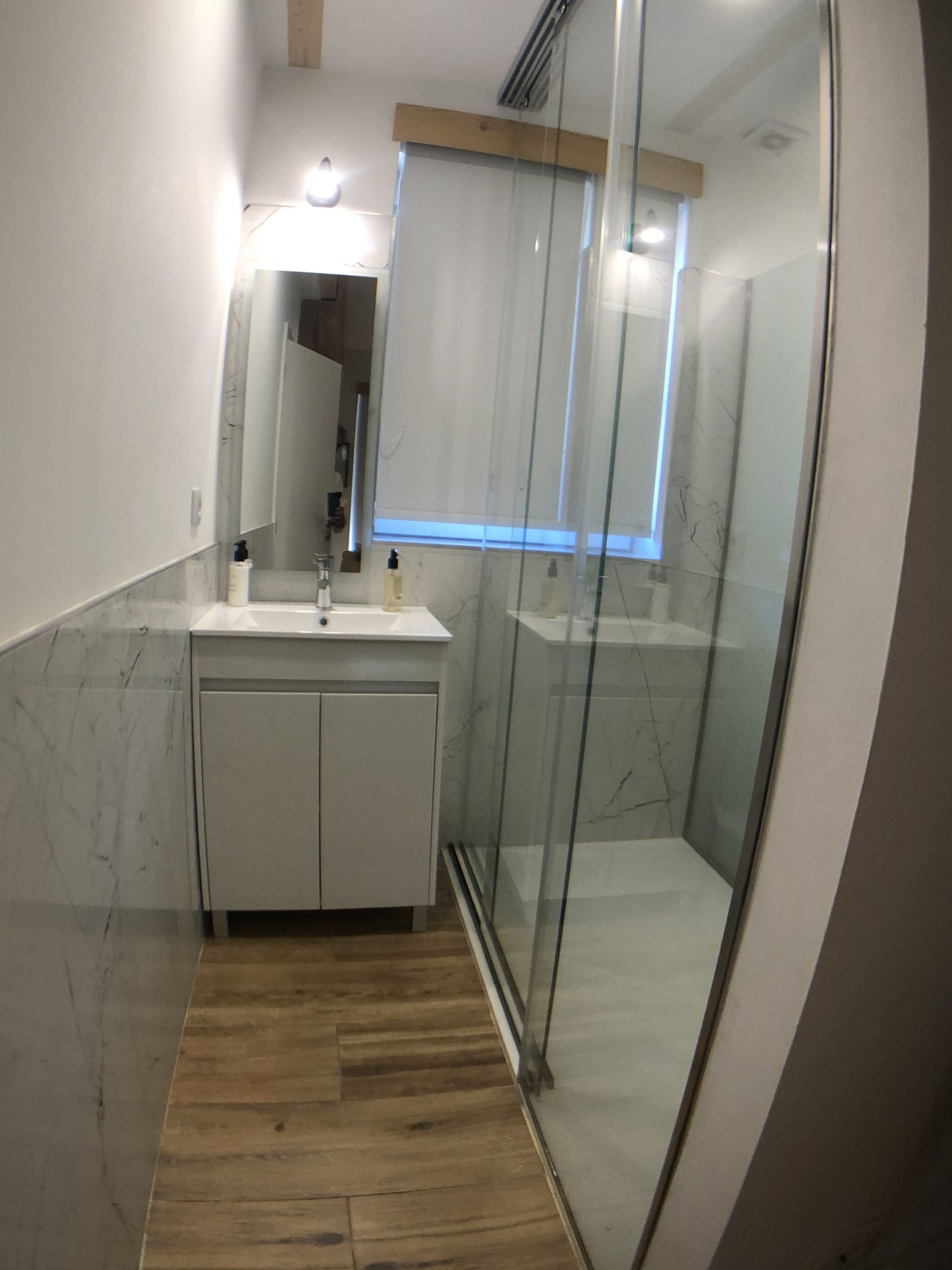 A modern bathroom with a glass shower enclosure, a wooden floor, and a marble backsplash.