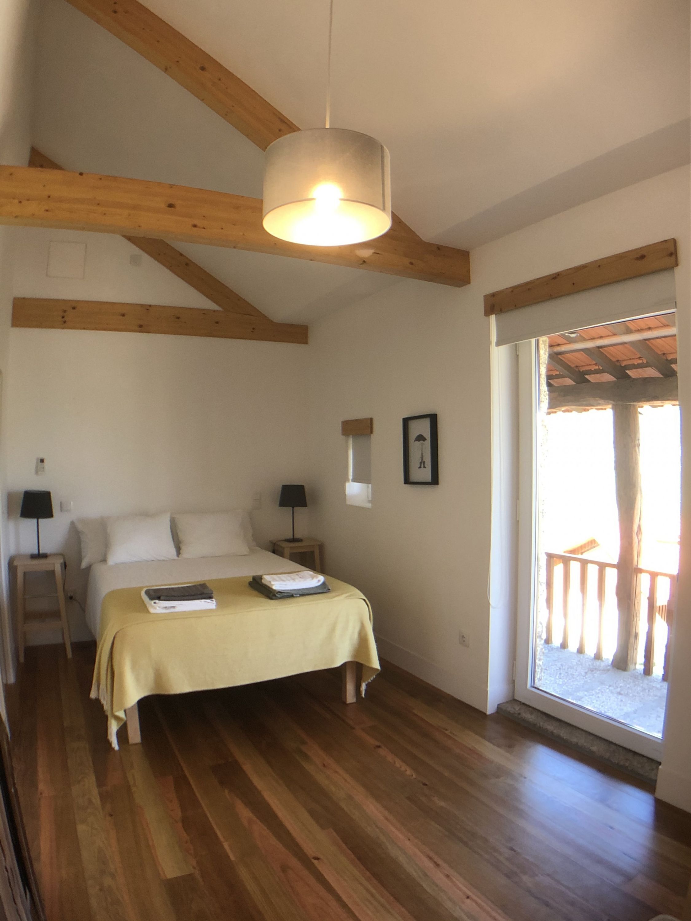 Un dormitorio con cama, mesitas de noche, lámpara colgante y ventana con vista al exterior.
