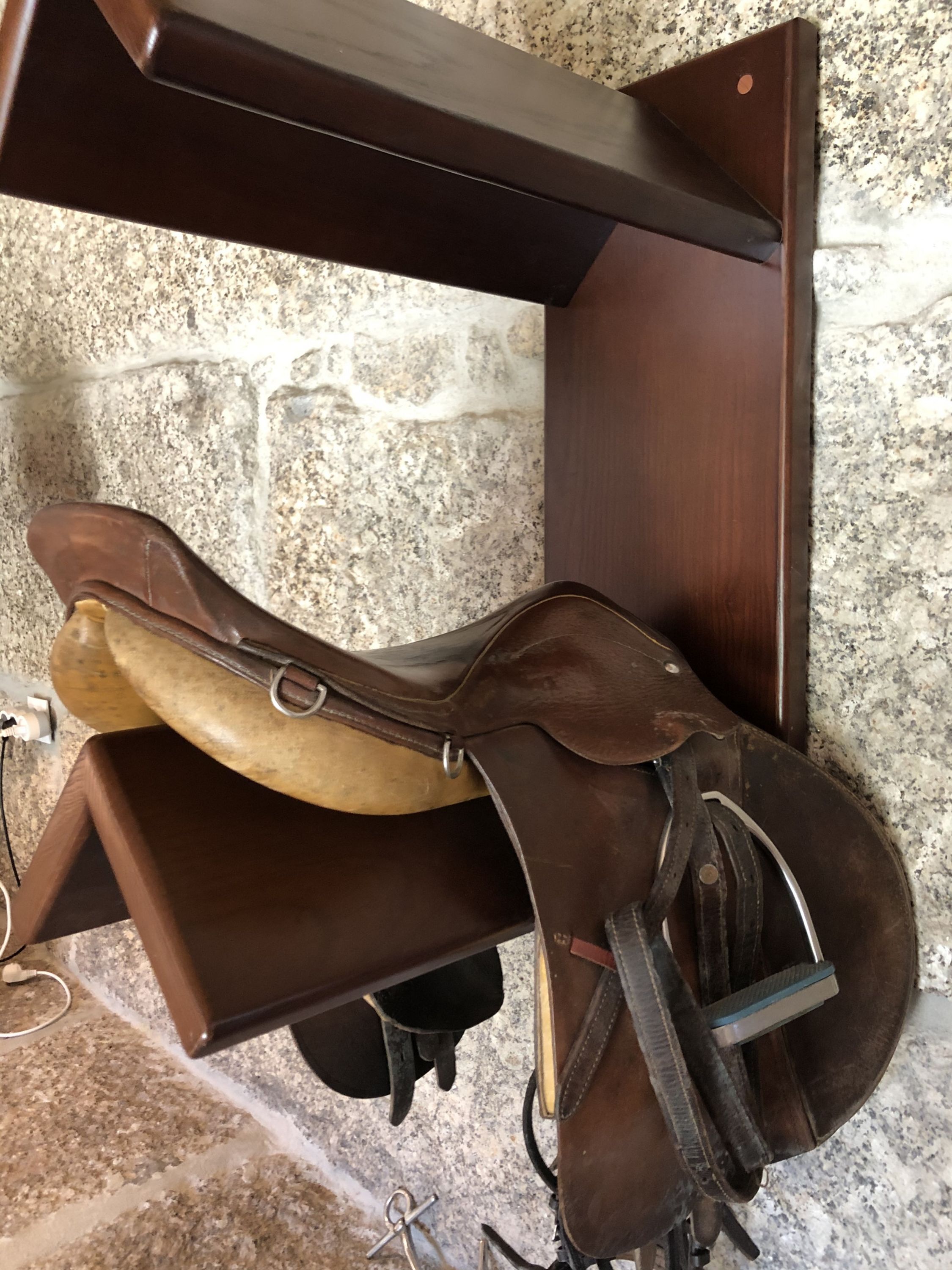 Een houten zadel voor paard bevestigd aan een muur, met een stenen muur op de achtergrond.
