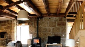 A cozy living room with a stone fireplace, a sofa, a television, and a wooden ceiling. - Vila Forno in Bustelo (Penafiel)