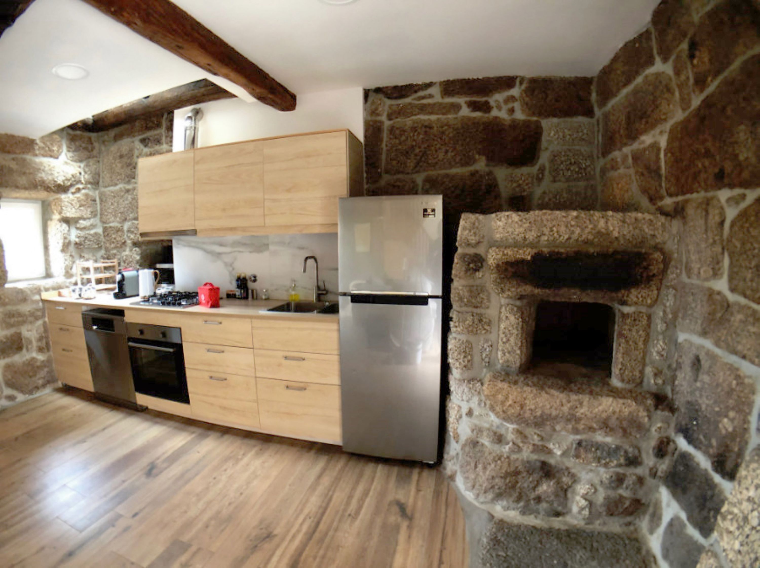 A kitchen with wooden cabinets, a stainless steel refrigerator, a dishwasher, and a stone wall oven.