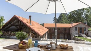 A wooden table set outdoors with a table umbrella, a basket of fruits, a bottle of juice, and a pitcher of milk. - Vila Beiral in Penafiel (Penafiel)