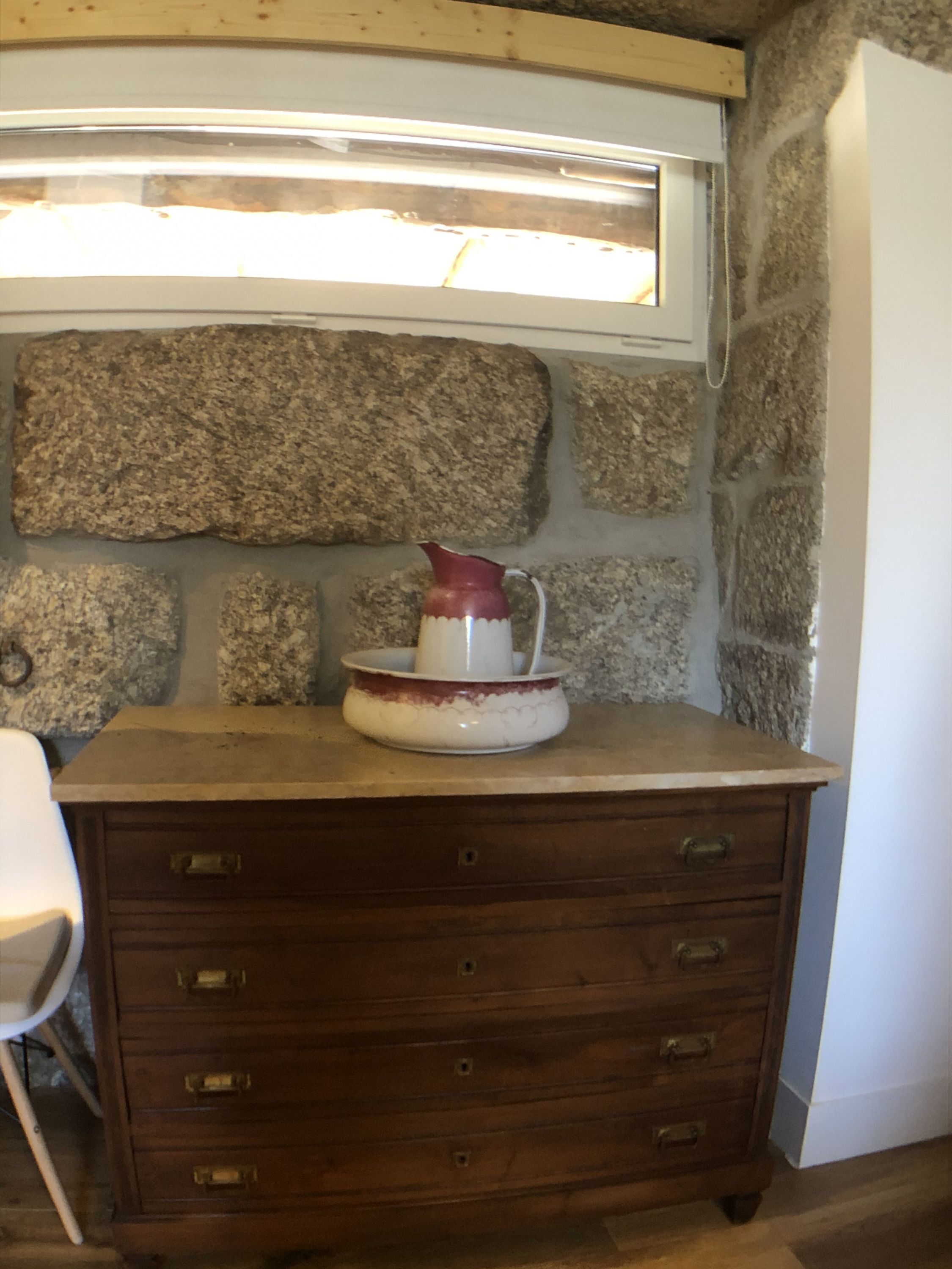 A kitchen with a stone wall, a wooden cabinet, and a white pitcher on the counter.