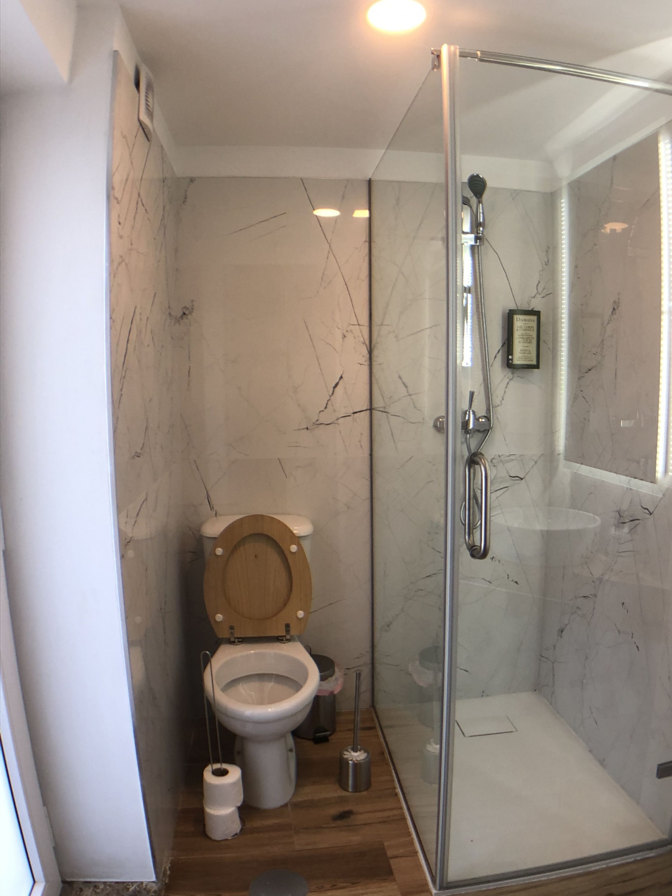 A modern bathroom with a glass-enclosed shower, a wooden toilet, and marble walls.