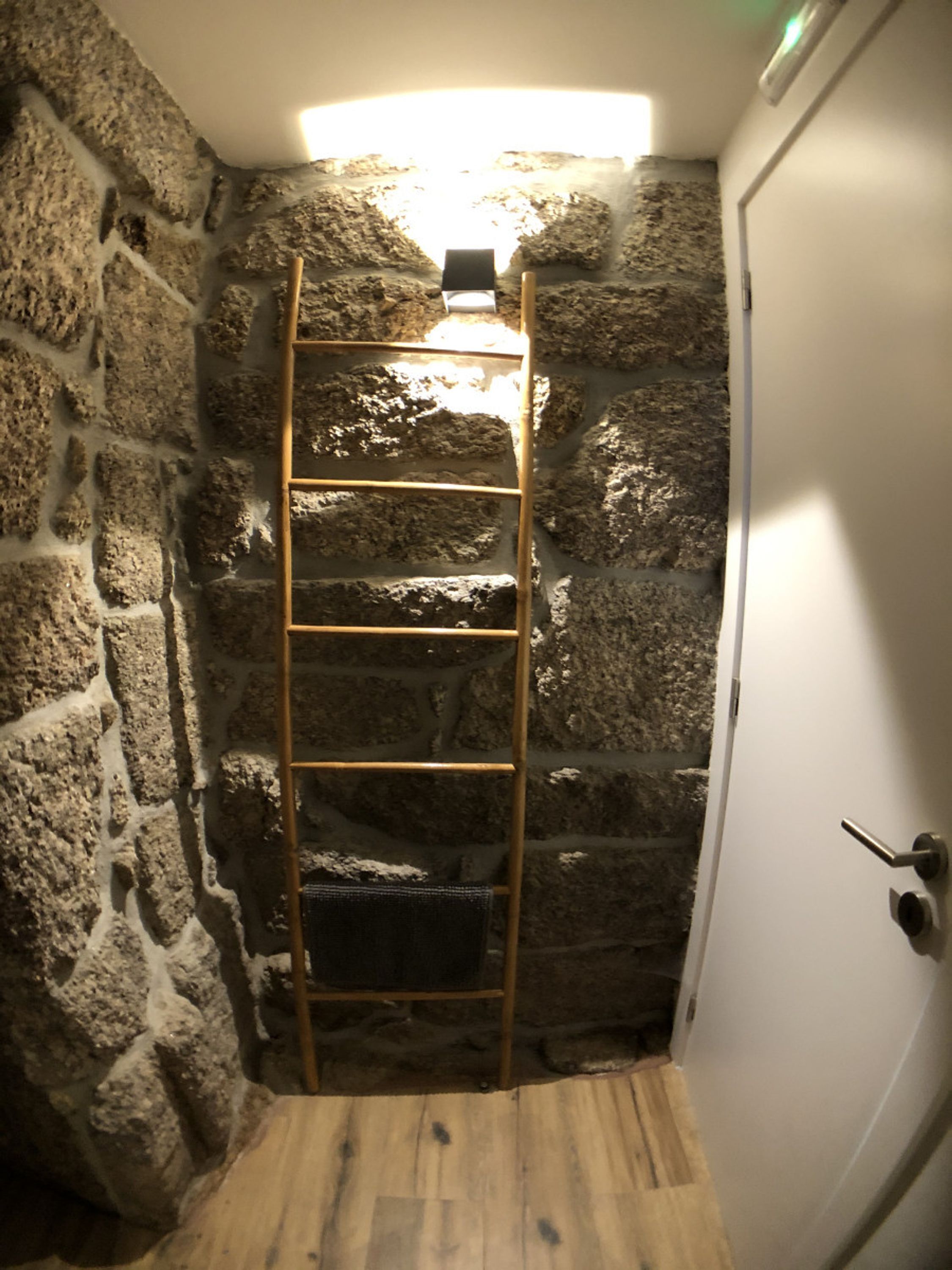 Una habitación estrecha con paredes de piedra y una escalera de madera que lleva a una pequeña abertura.