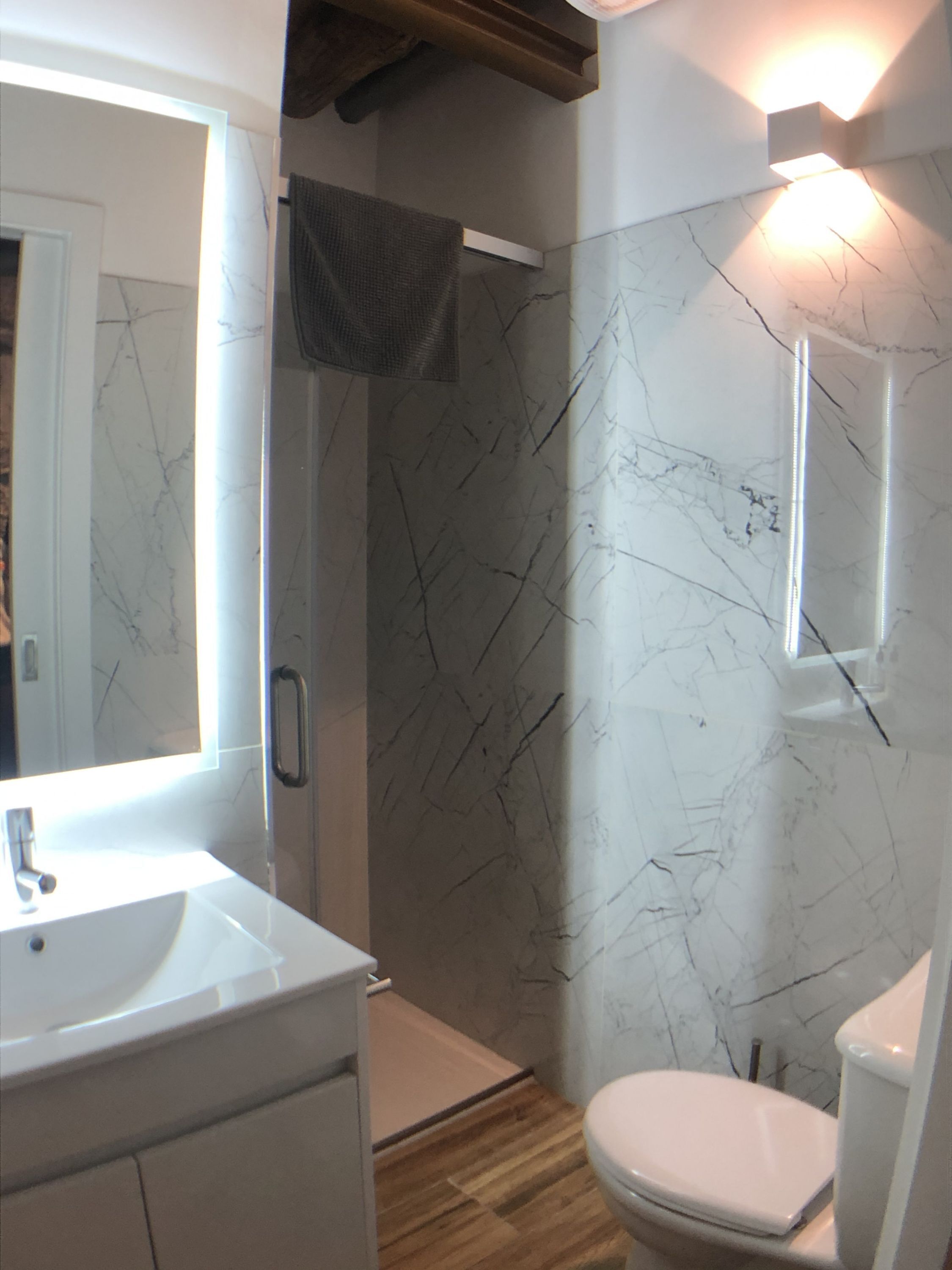 A bathroom with a marble wall, a white sink, a toilet, and a shower area.