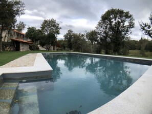 A rectangular swimming pool with a stone edge, surrounded by a grassy lawn and trees.