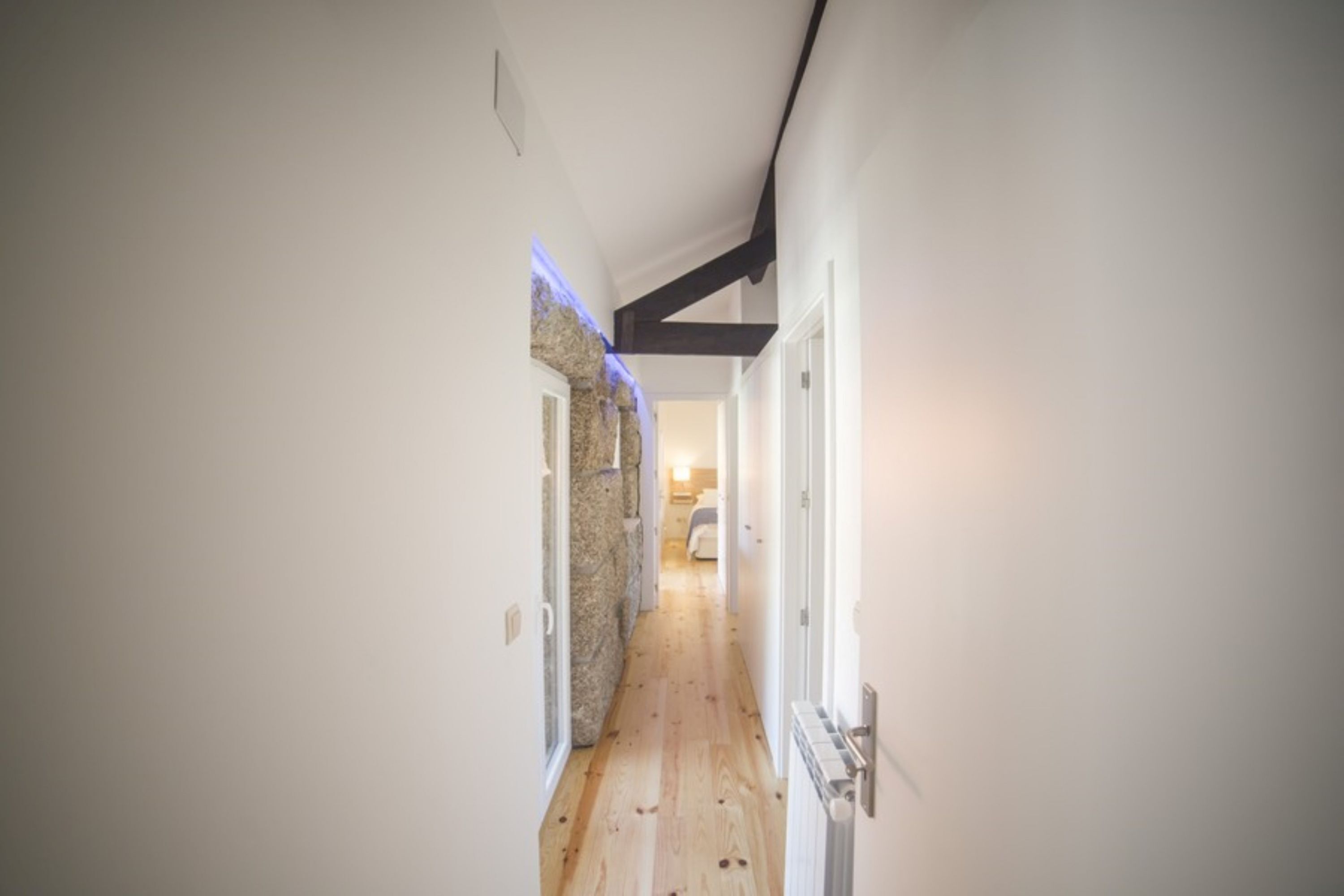 A narrow hallway with wooden flooring, white walls, and a stone accent wall.