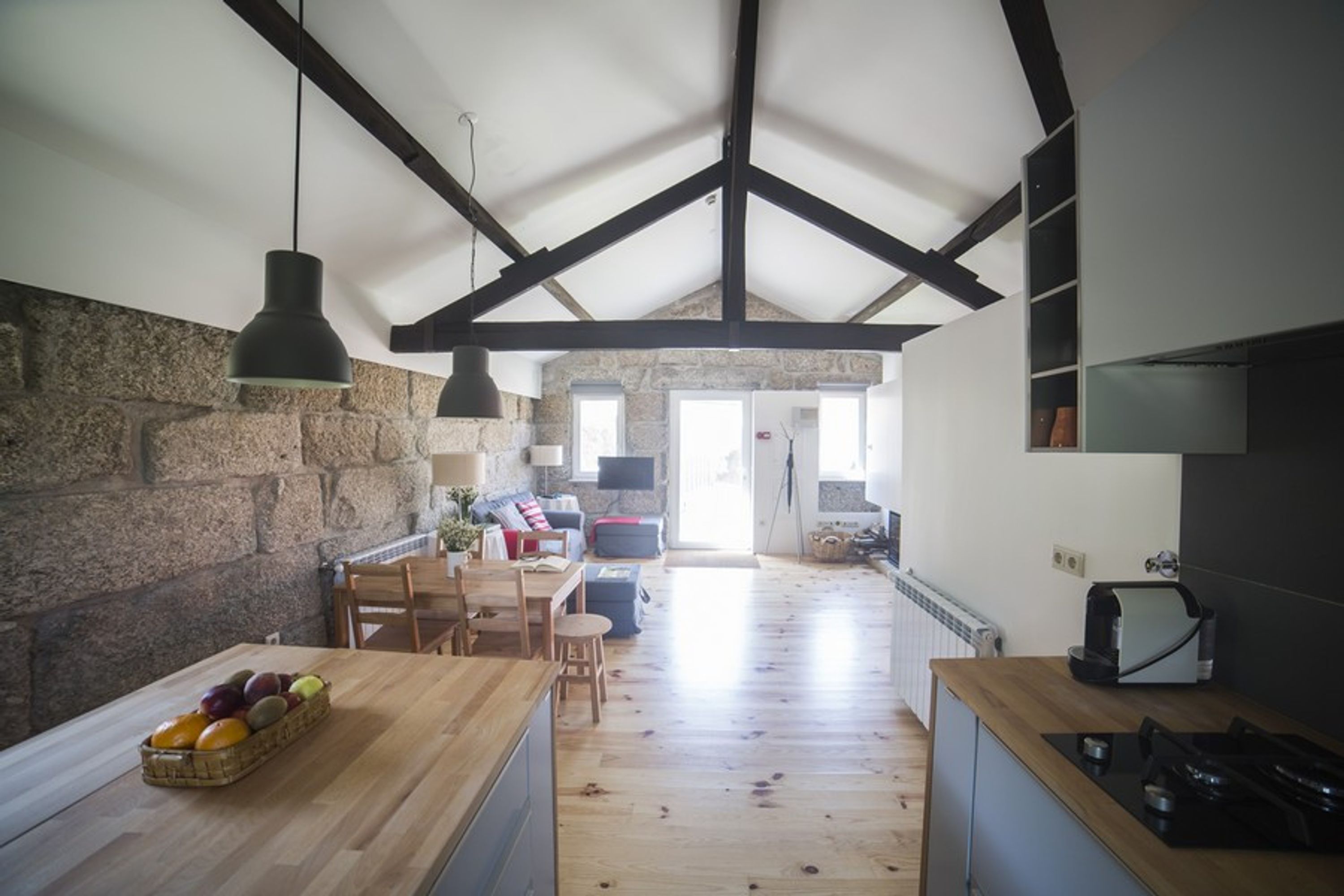 A spacious kitchen with wooden flooring, a stone wall, and a high ceiling with exposed beams.