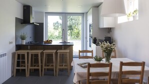 Eine moderne Küche mit einer zentralen Kochinsel, Holzbarhocker, einem Esstisch mit Stühlen und einem großen Fenster für natürliches Licht.