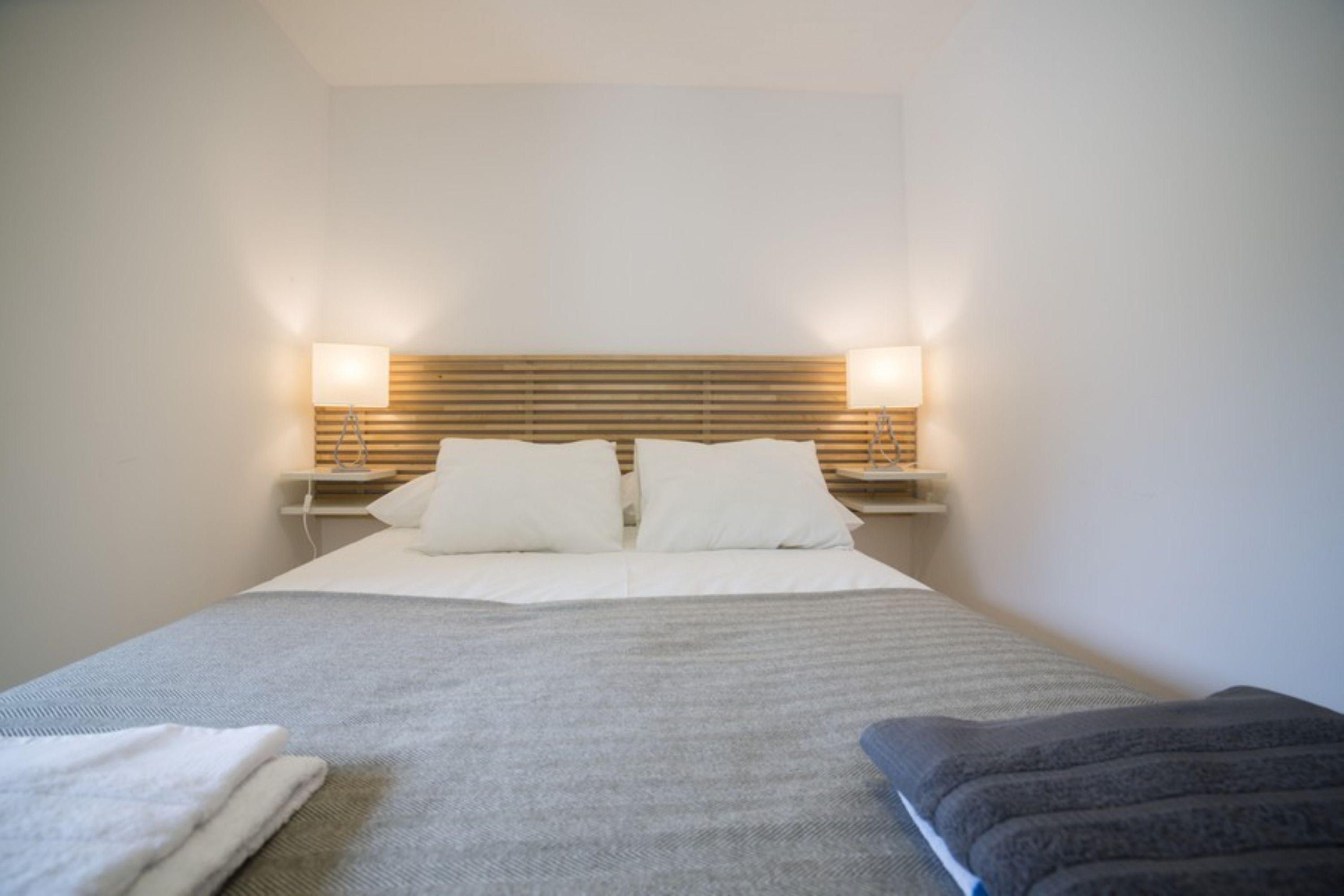 A neatly made bed with white linens and two pillows, flanked by bedside lamps on either side.