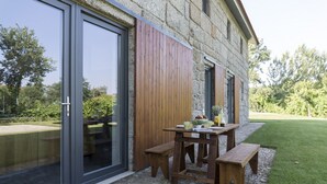Ein Steinhaus mit einer Holzterrasse, einem Tisch mit Bänken und einer Glastür.