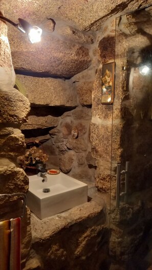 Un baño con paredes de piedra, un lavamanos y una ducha.