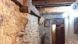 A stone-walled hallway with a tiled floor, a wooden ceiling, and a table with a vase of flowers. - New Riyork Sweet Home (Montalegre)