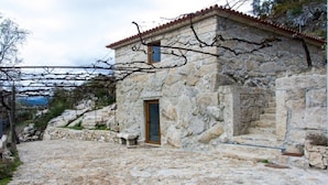 A stone building with a tiled roof, a wooden door, and a stone staircase leading to the entrance. - New Riyork Sweet Home (Montalegre)