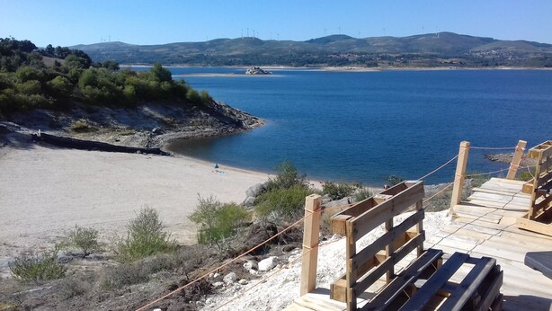 A beach with wooden benches and a clear view of the sea and distant hills. - New Riyork Sweet Home (Montalegre)