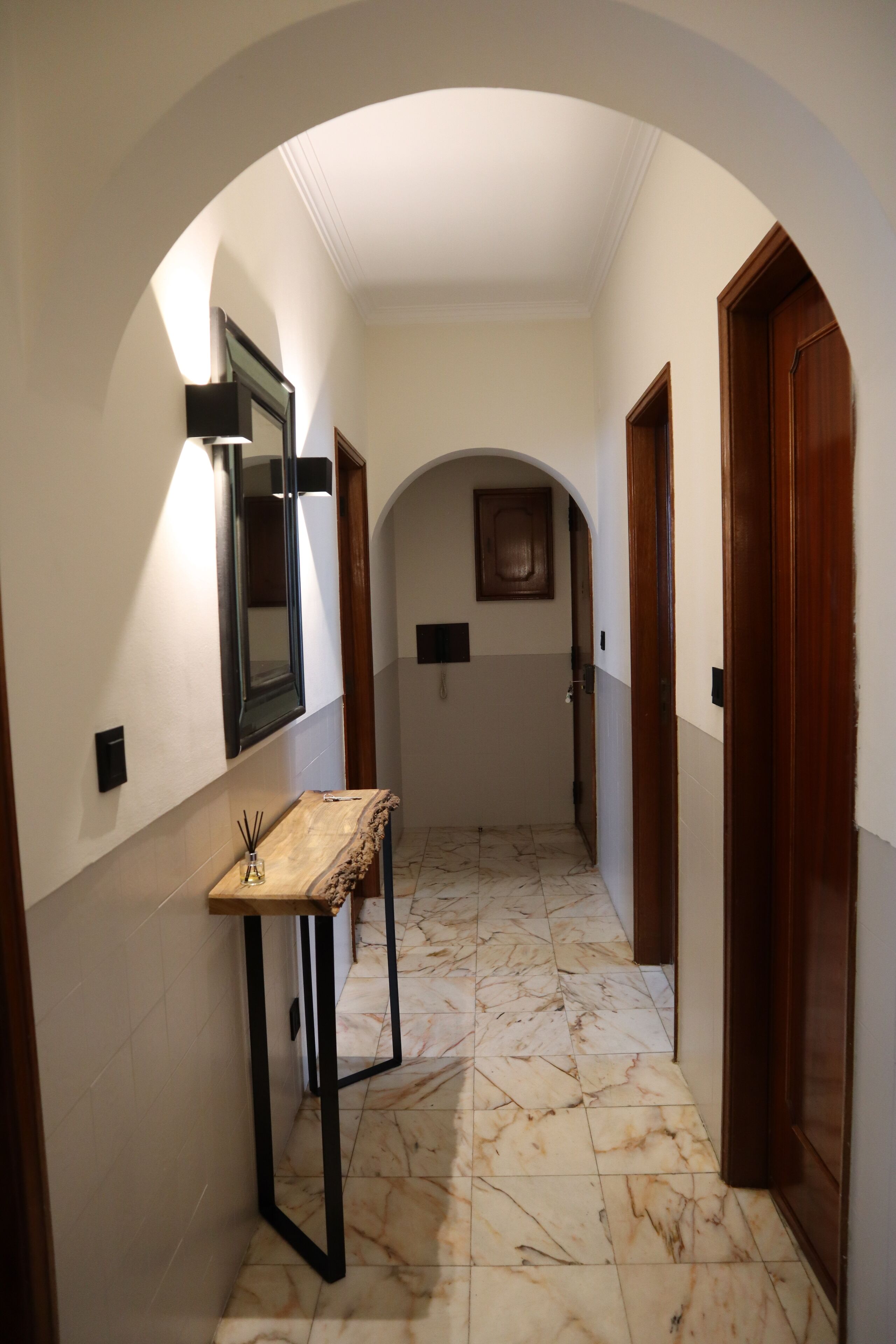 A hallway with a marble floor, a wooden bench, a mirror, and two doors.