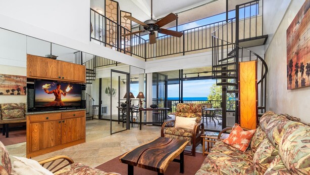 A spacious living area with a large TV, wooden furniture, and a balcony with a view. - 🏖️Top-Floor Ocean View Condo w/ A/C + Loft (Kailua Kona)