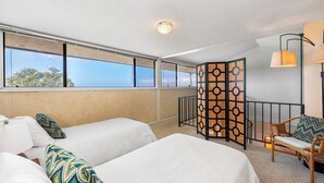A hotel room with two beds, a view of the sea, a balcony with a railing, and a chair with a cushion. - 🏖️Top-Floor Ocean View Condo w/ A/C + Loft (Kailua Kona)