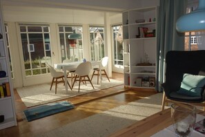 Un salón luminoso con zona de comedor, ventanas amplias y una estantería.