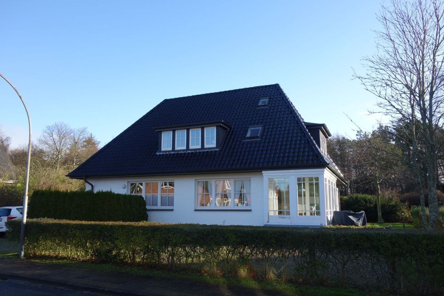 Ein zweistöckiges Haus mit dunklem Dach, weißen Außenwänden und mehreren Fenstern.