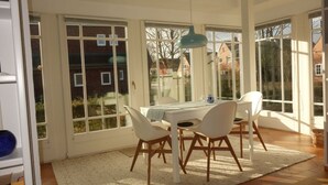 A dining area with a table and chairs, large windows, and a hanging light fixture.