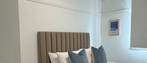 A bedroom with a bed, pillows, a bedside table, a remote control, and a framed picture on the wall.