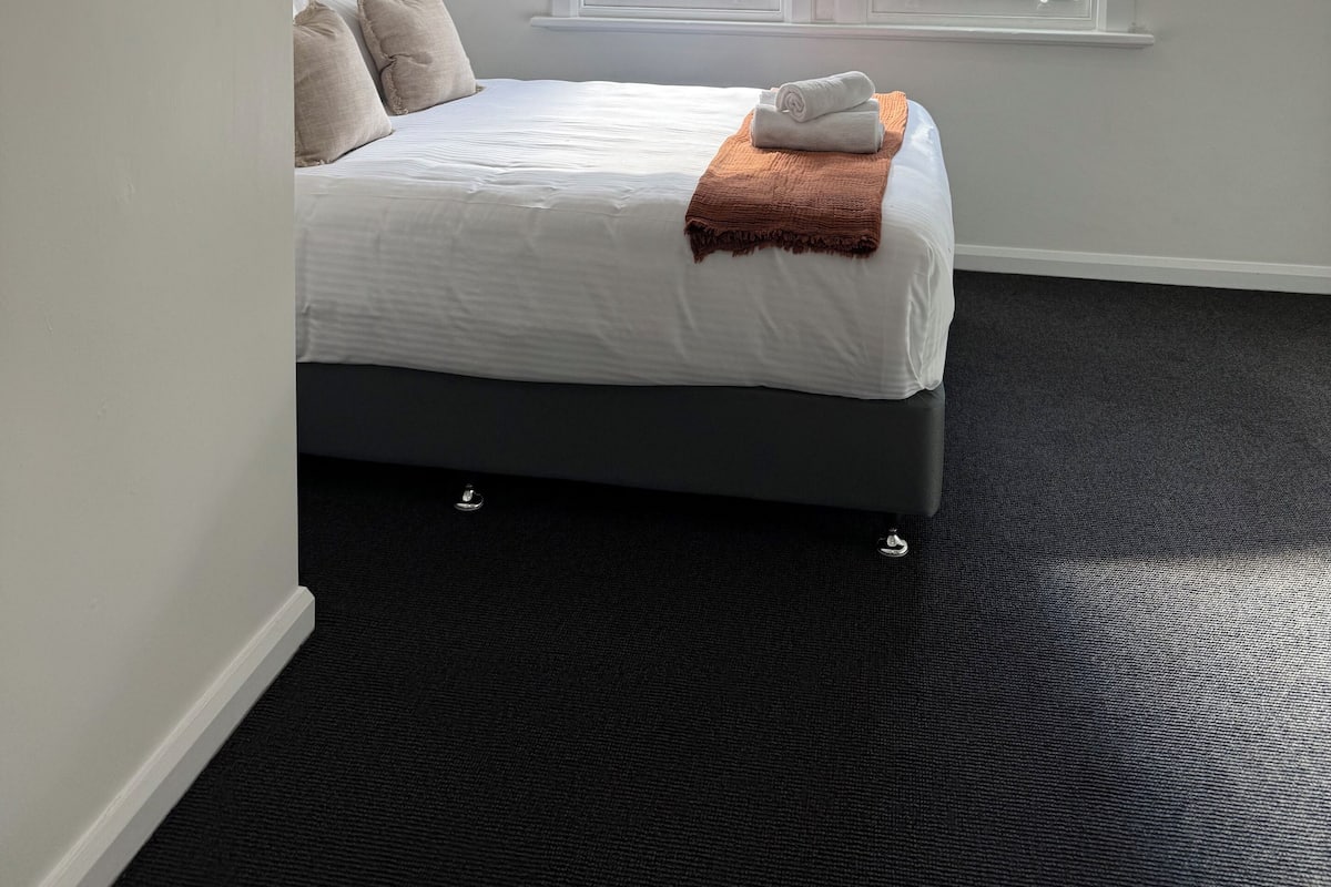 Une chambre d’hôtel avec un lit, un ventilateur de plafond, une fenêtre avec des stores et un sol recouvert de moquette.